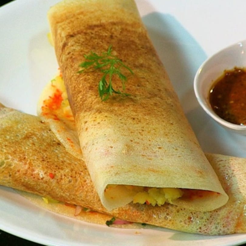 Two golden-brown dosas, one rolled and one open, filled with potato masala, served with chutney.