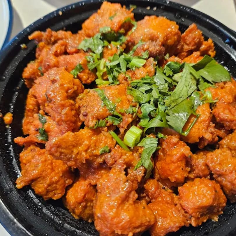 Annapoorani's Chicken 65, a vibrant red Indian fried chicken dish garnished with fresh green herbs.