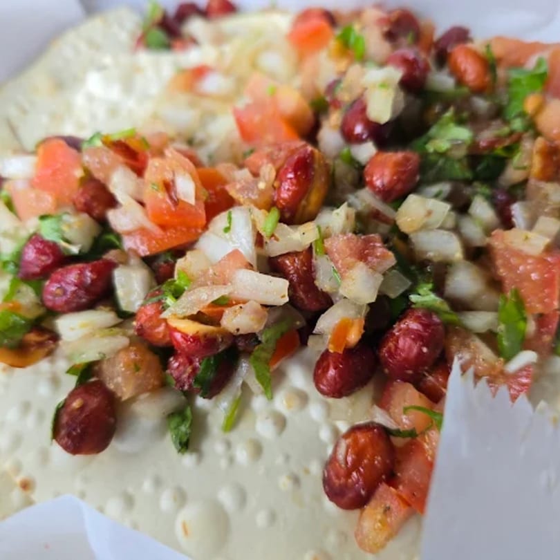 Close-up of an Indian dish with red beans, diced tomatoes, onions, and herbs on a flatbread.