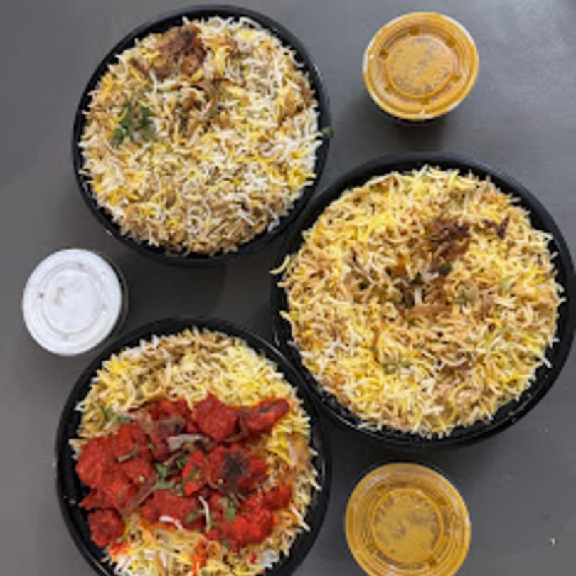 Three bowls of Annapoorani Indian biryani, one with red chicken, and two small sauce containers.