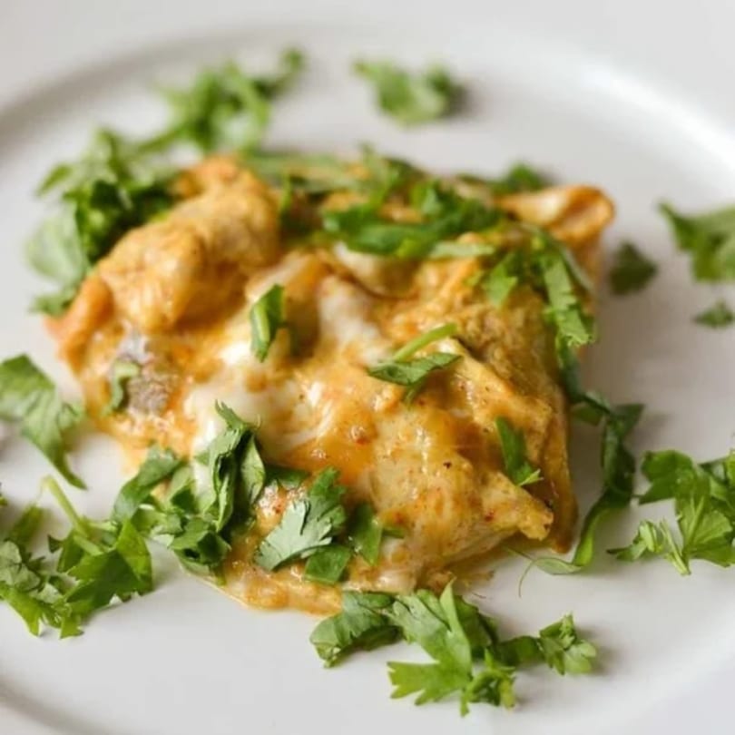 Indian dish with a creamy orange sauce and fresh green herbs on a white plate.