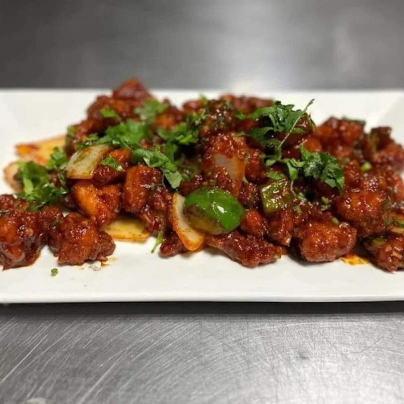 Annapoorani's chili chicken, a vibrant Indian dish with red sauce, green peppers, and cilantro.